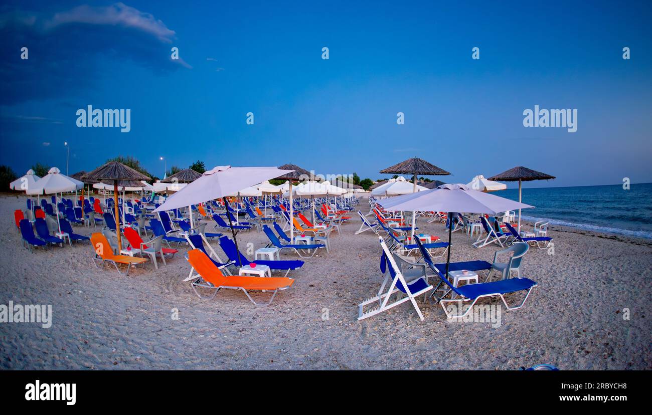 La plage est pleine de transats colorés avant le coucher du soleil en Grèce. Transats orange, rouge et bleu. Banque D'Images