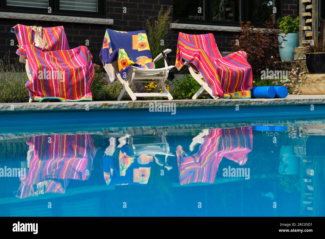 Serviettes de plage rose reflétées dans l'eau de piscine bleu calme dans l'arrière-cour avec jardin à côté de la maison Banque D'Images