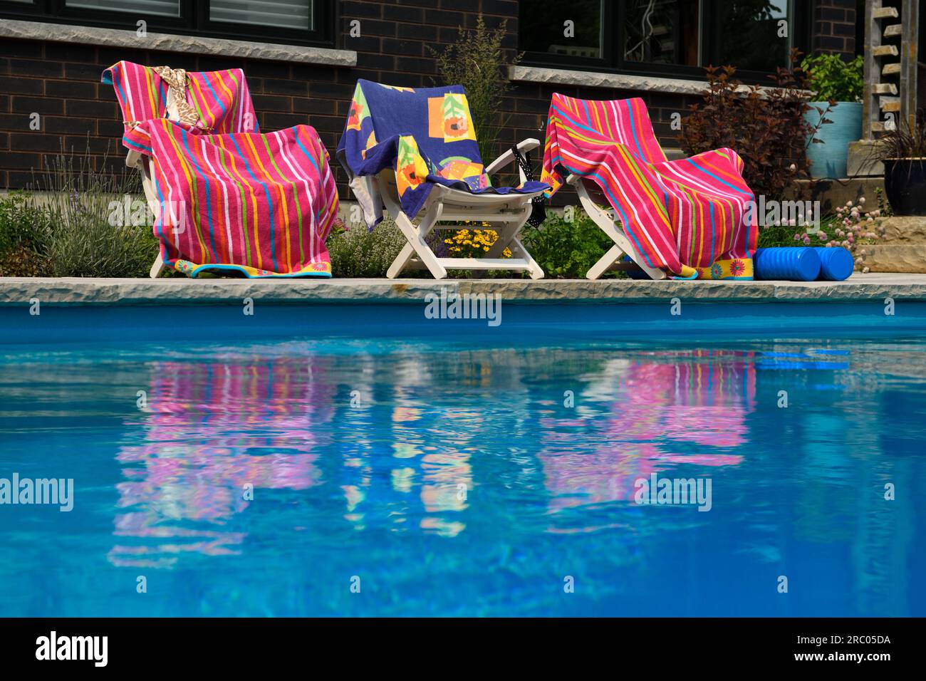 Serviettes de plage rose reflétées dans l'eau de piscine bleue ondulante dans la cour avec jardin Banque D'Images