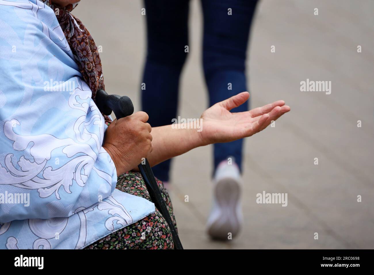 Mendiante vieille femme demande l'aumône assise dans une rue de la ville avec la main tendue. Pauvreté, sans-abri et concept de mendicité Banque D'Images