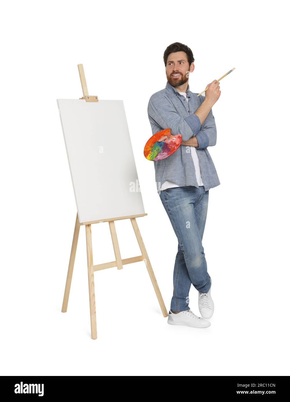 Homme heureux avec pinceau et palette de l'artiste près du chevalet avec toile sur fond blanc. Passe-temps créatif Banque D'Images