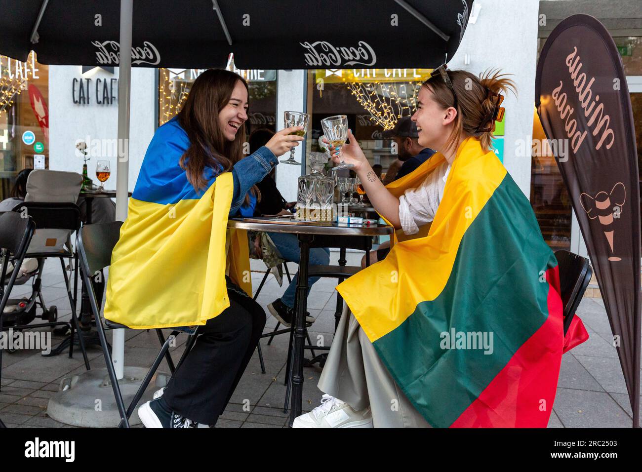 Vilnius, Lituanie. 11 juillet 2023. Des étudiants lituaniens enveloppés de drapeaux nationaux ukrainiens et lituaniens sont assis dans un pub près du palais présidentiel à Vilnius. Le Président de la Lituanie organise le dîner des dirigeants mondiaux au Palais présidentiel. L'ordre du jour du sommet couvre la candidature de l'Ukraine à l'adhésion à l'organisation, le processus d'adhésion de la Suède, l'augmentation des stocks d'armes et la révision des plans. Crédit : SOPA Images Limited/Alamy Live News Banque D'Images