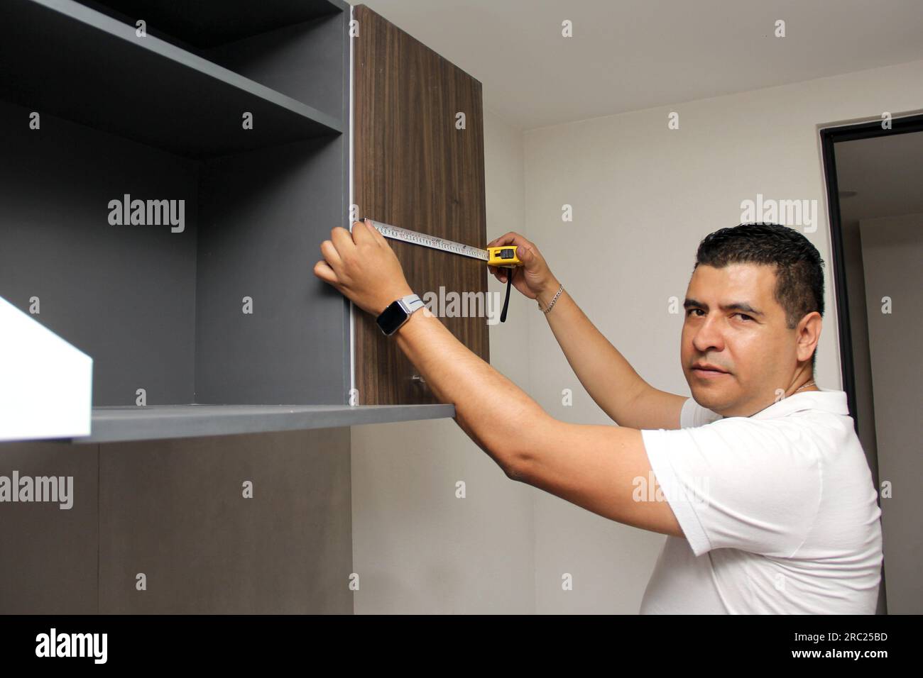 Un homme latino-américain de 40 ans aux cheveux foncés prend des mesures d'armoires de cuisine nouvellement installées en tant que travailleur Banque D'Images