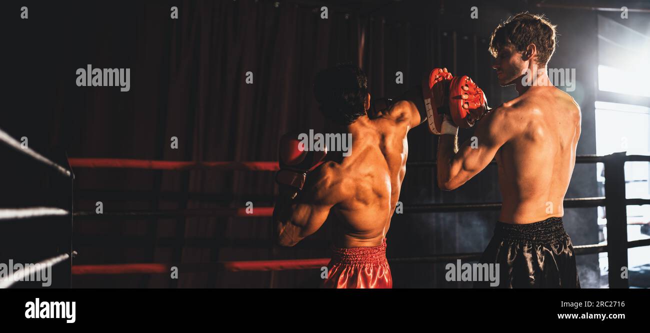 Le boxeur asiatique et caucasien Muay Thai lance une attaque au coude dans une séance d'entraînement de boxe féroce, livrant une frappe au coude à l'entraîneur sparring, mettant en vedette Banque D'Images
