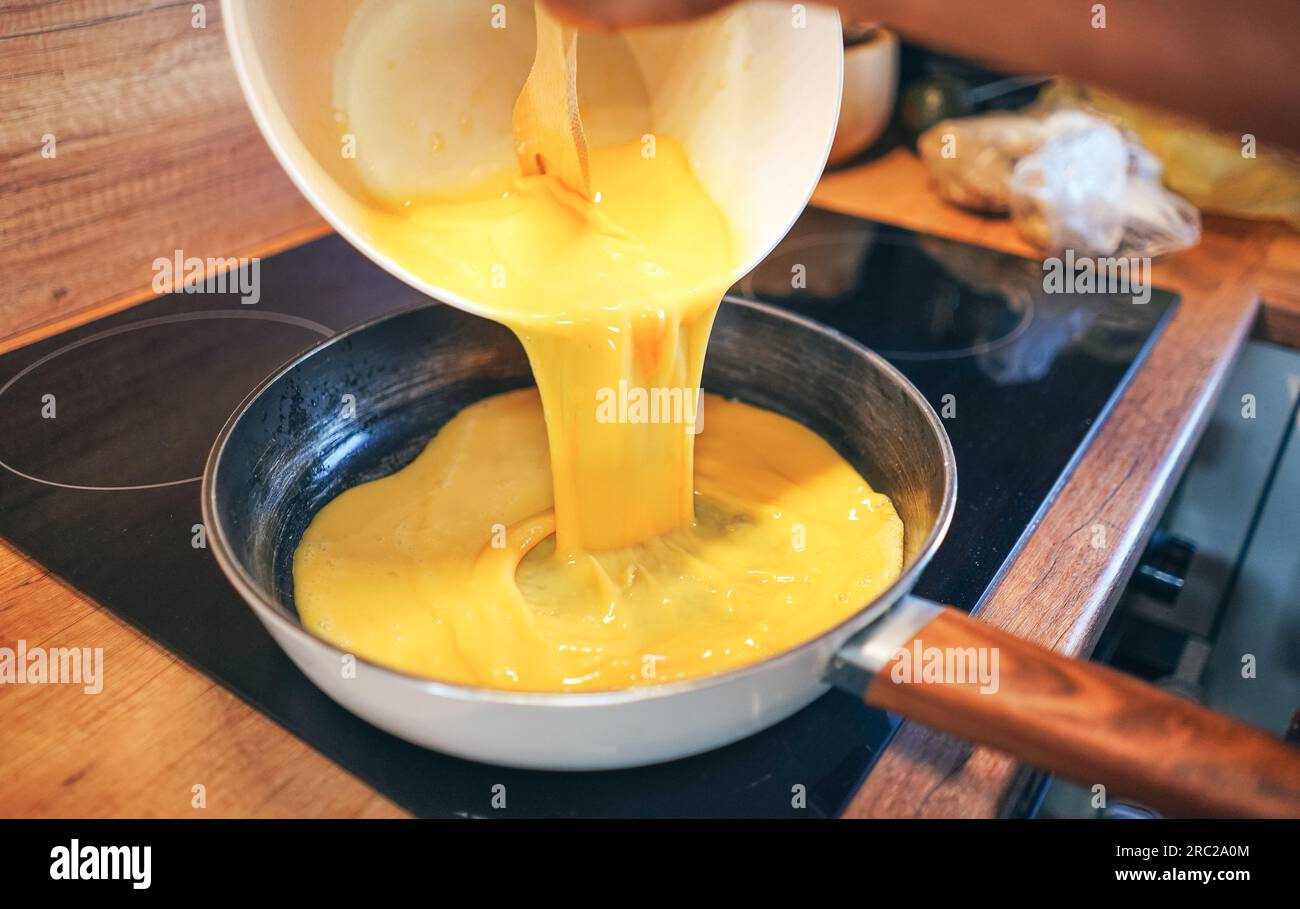 Oeufs brouillés. Chef versant des œufs liquides sur une poêle chaude. Faire des œufs brouillés. Banque D'Images