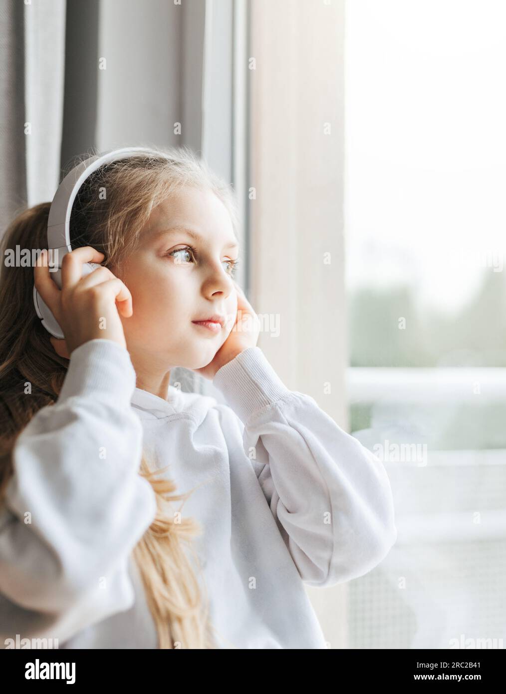 Petite fille avec des écouteurs à l'intérieur à la maison, assis sur le rebord de la fenêtre et écouter de la musique Banque D'Images