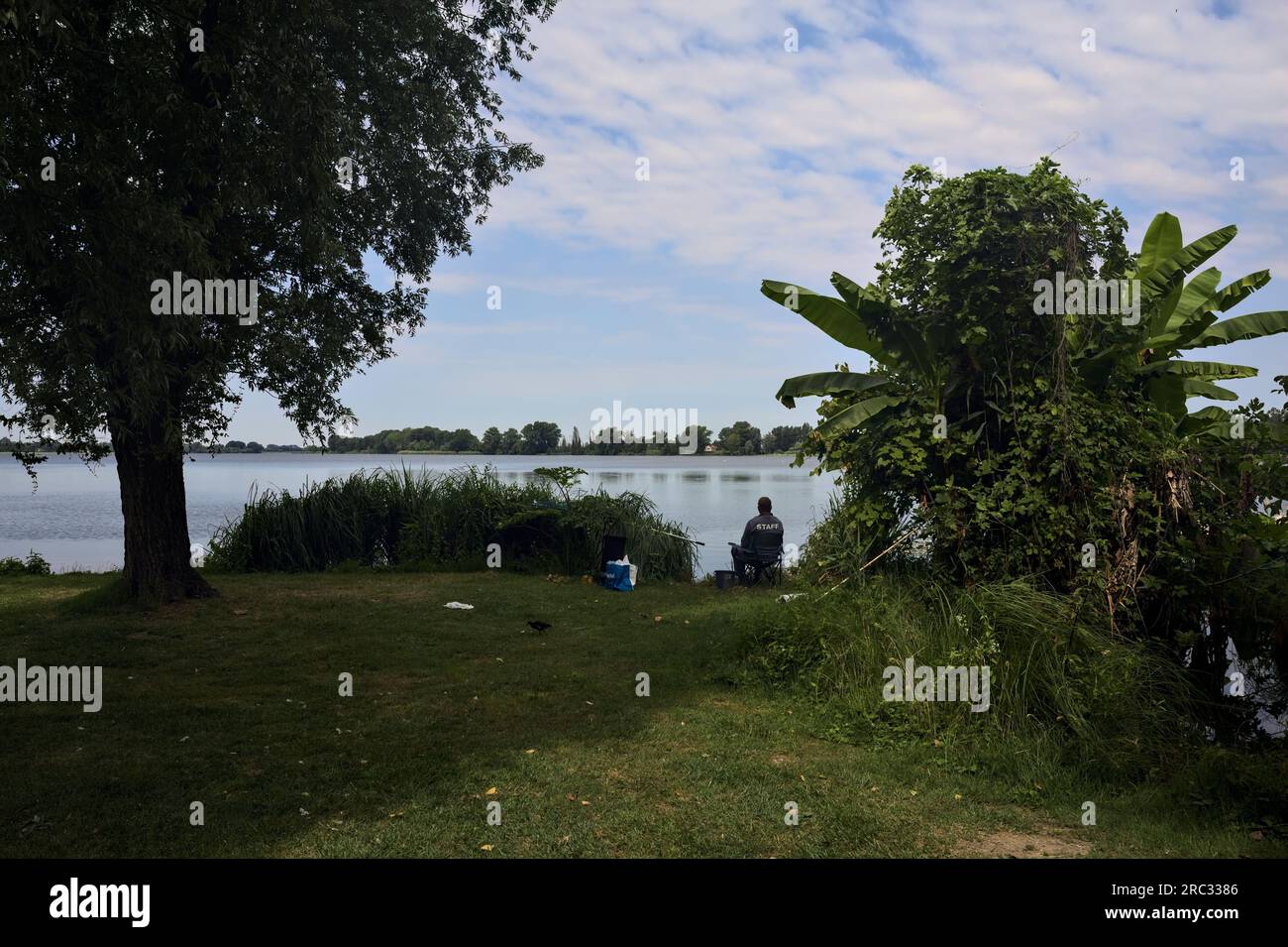 Lakeshore avec des arbres et un pêcheur assis sur une journée ensoleillée dans la campagne italienne Banque D'Images