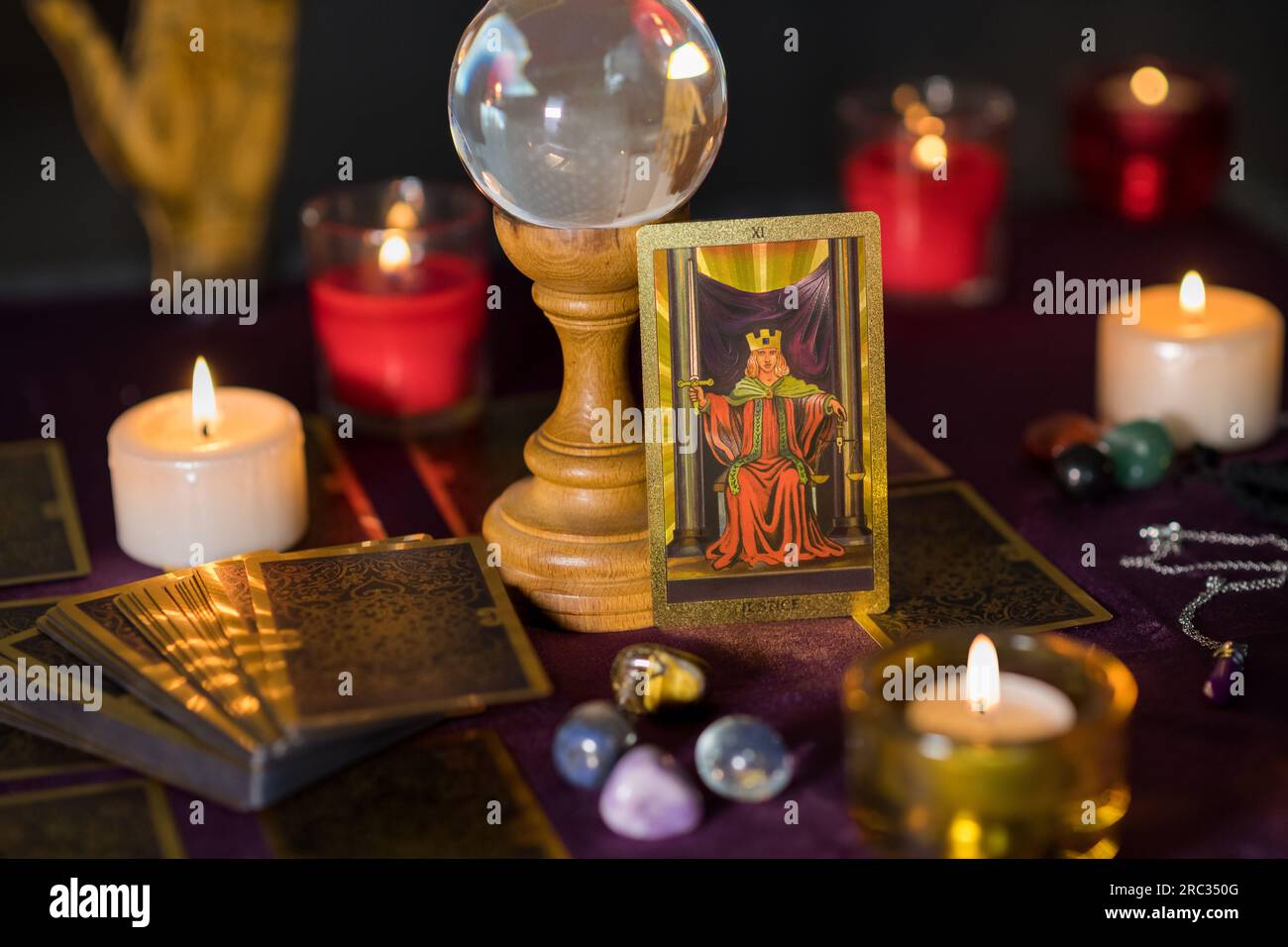 Carte de tarot de justice avec jeu de cartes placé sur la table près de l'ensemble de bougies allumées avec boule de cristal de verre et pierres Banque D'Images