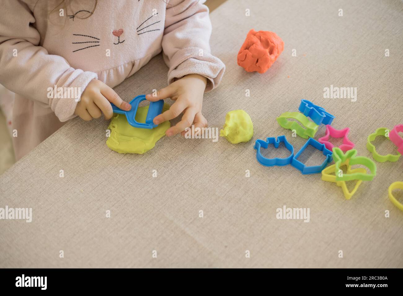 Enfant caucasien, deux ou trois ans, jouant et exerçant la motricité fine avec ses mains, avec de l'argile et de la plasticine colorée. Banque D'Images