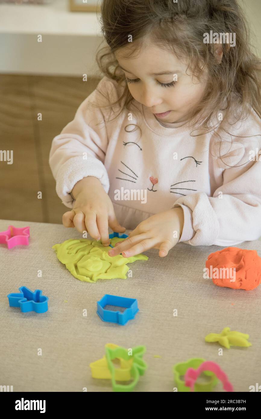 Enfant caucasien, deux ou trois ans, jouant et exerçant la motricité fine avec ses mains, avec de l'argile et de la plasticine colorée. Banque D'Images