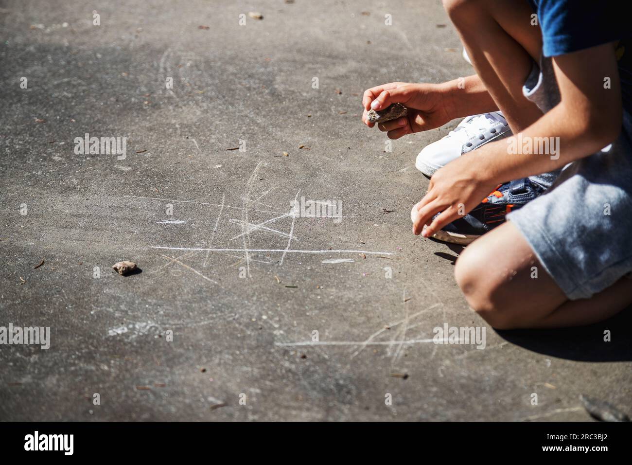 Enfance heureuse. Enfants caucasiens jouant dehors pendant la journée, grattant le sol avec une roche pour jouer le jeu classique de TIC-tac-toe. Banque D'Images