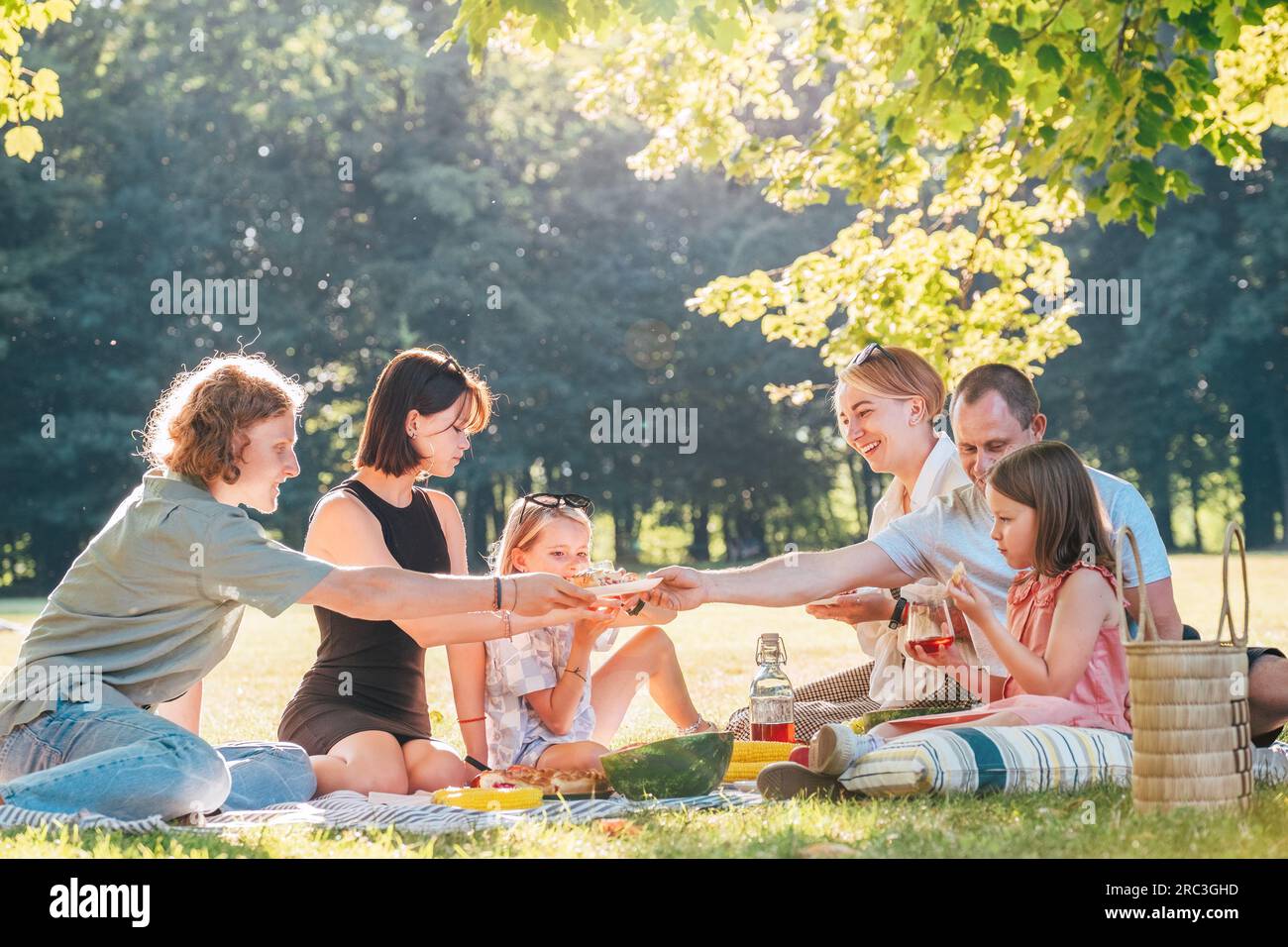 Grande famille assis sur la couverture de pique-nique dans le parc de la ville pendant le week-end dimanche journée ensoleillée. Ils sourient, rient et mangent de la tarte avec du thé froid. Famille Banque D'Images