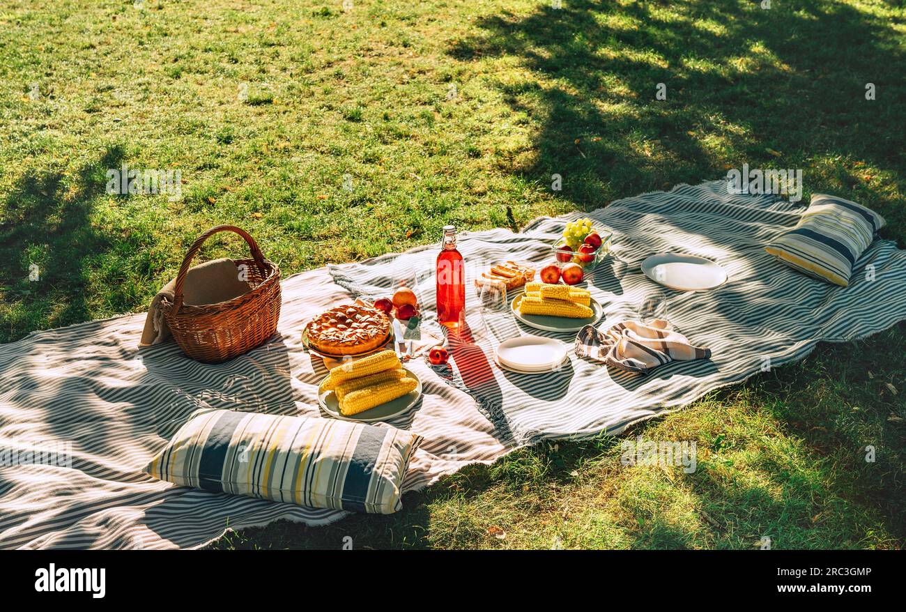 Couverture de pique-nique avec maïs bouilli, fruits, tarte juste soutenue, une bouteille de jus, nature morte panier dans le parc d'été de la ville. Personne. Banque D'Images