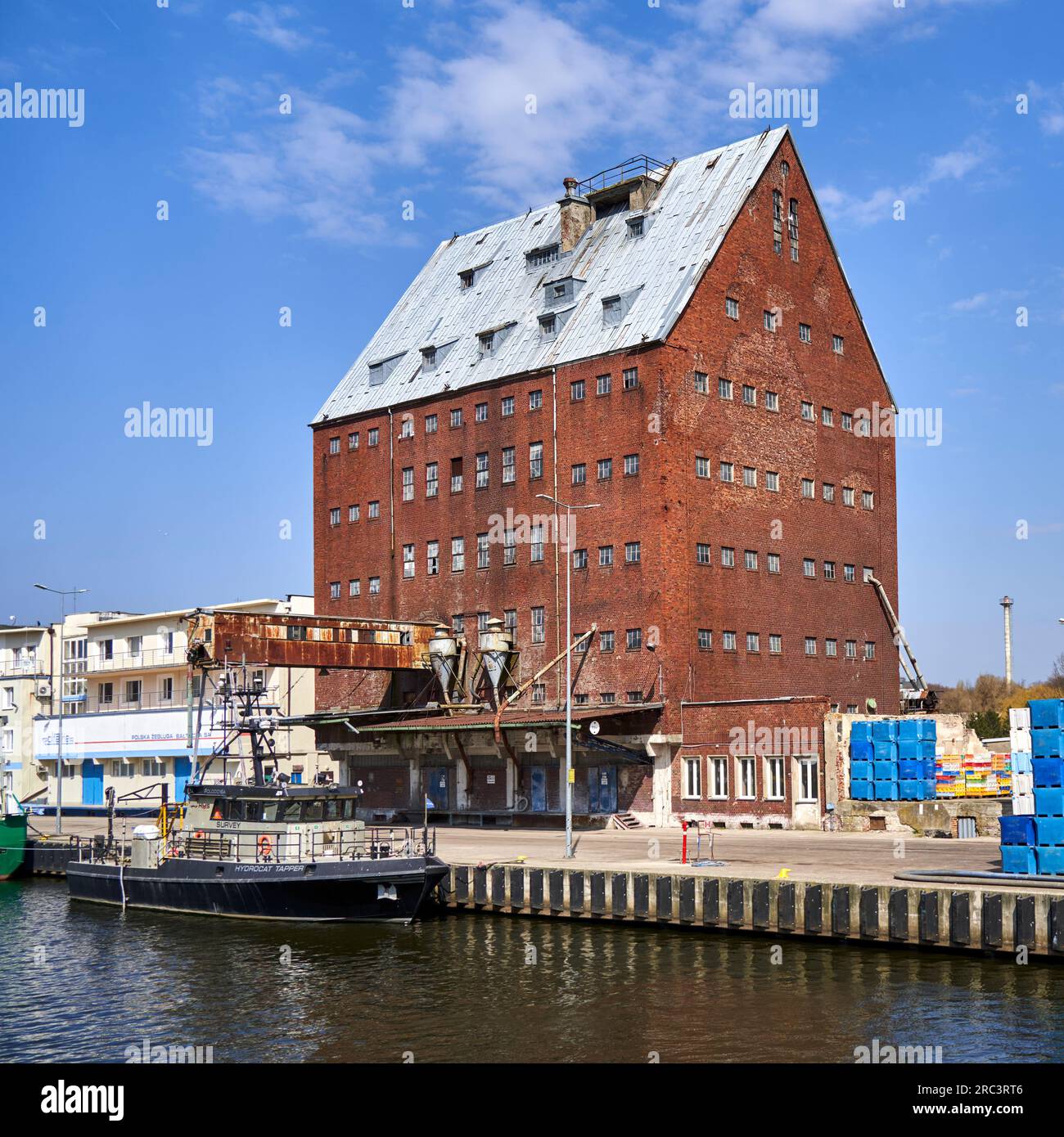 Kolberg, Pologne, 20 avril 2023 : silo historique de stockage en briques rouges avec quai et navire dans le port de la ville polonaise de Kołobrzeg Banque D'Images