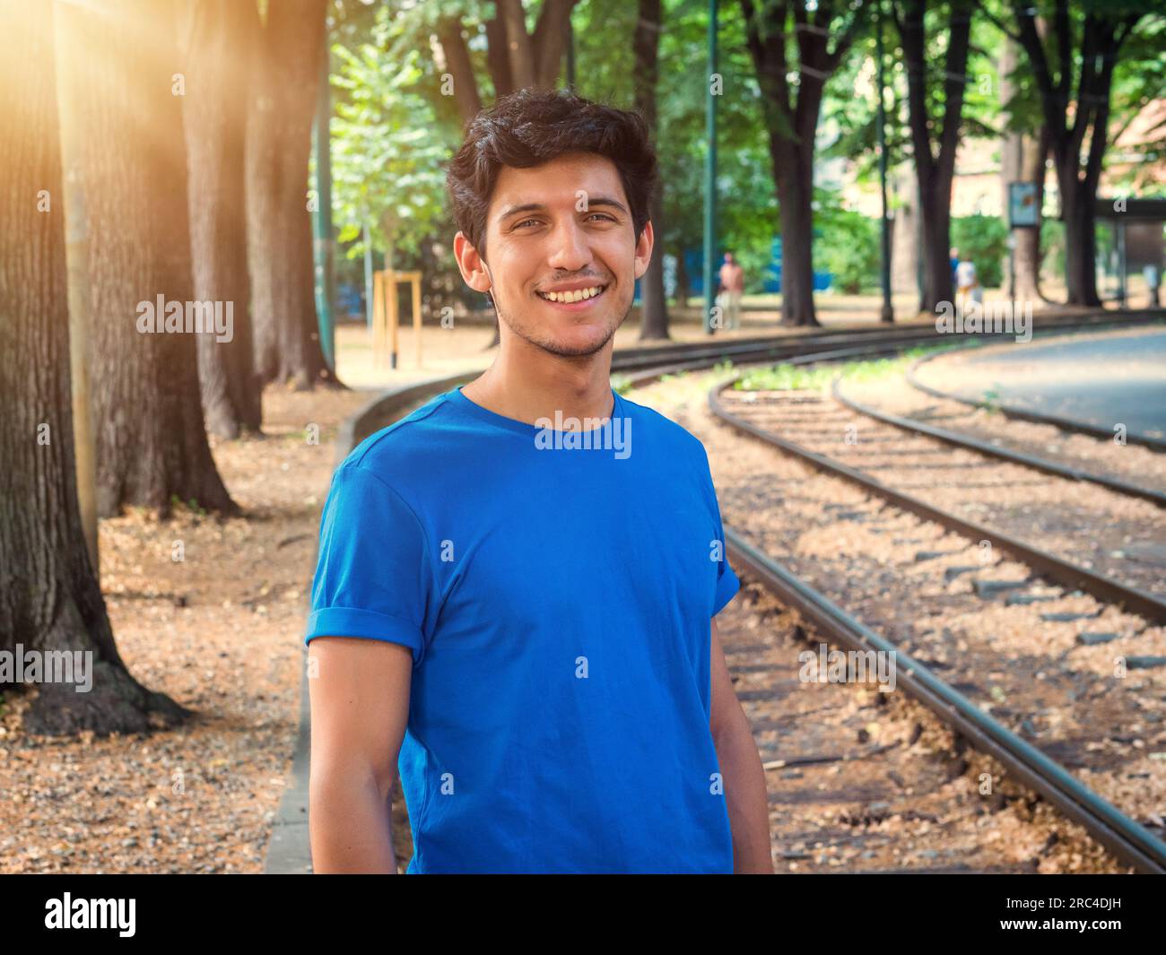 Vue de trois quarts d'un beau jeune homme en milieu urbain portant un polo bleu, souriant à la caméra Banque D'Images
