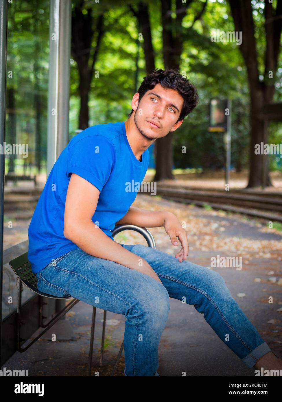 Photo de trois quarts d'un beau jeune homme en milieu urbain attendant le tram à l'arrêt de bus, portant un polo bleu Banque D'Images