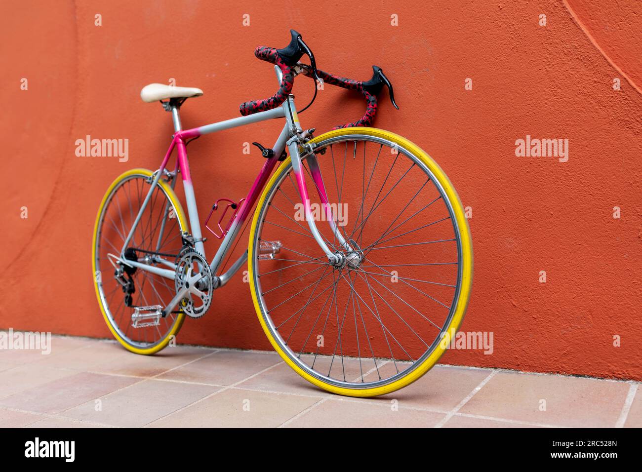 D'en haut de vélo de route moderne avec cadre rose bleu blanc siège pneus jaunes penchés sur le mur orange dans la rue sur le trottoir en été jour Banque D'Images