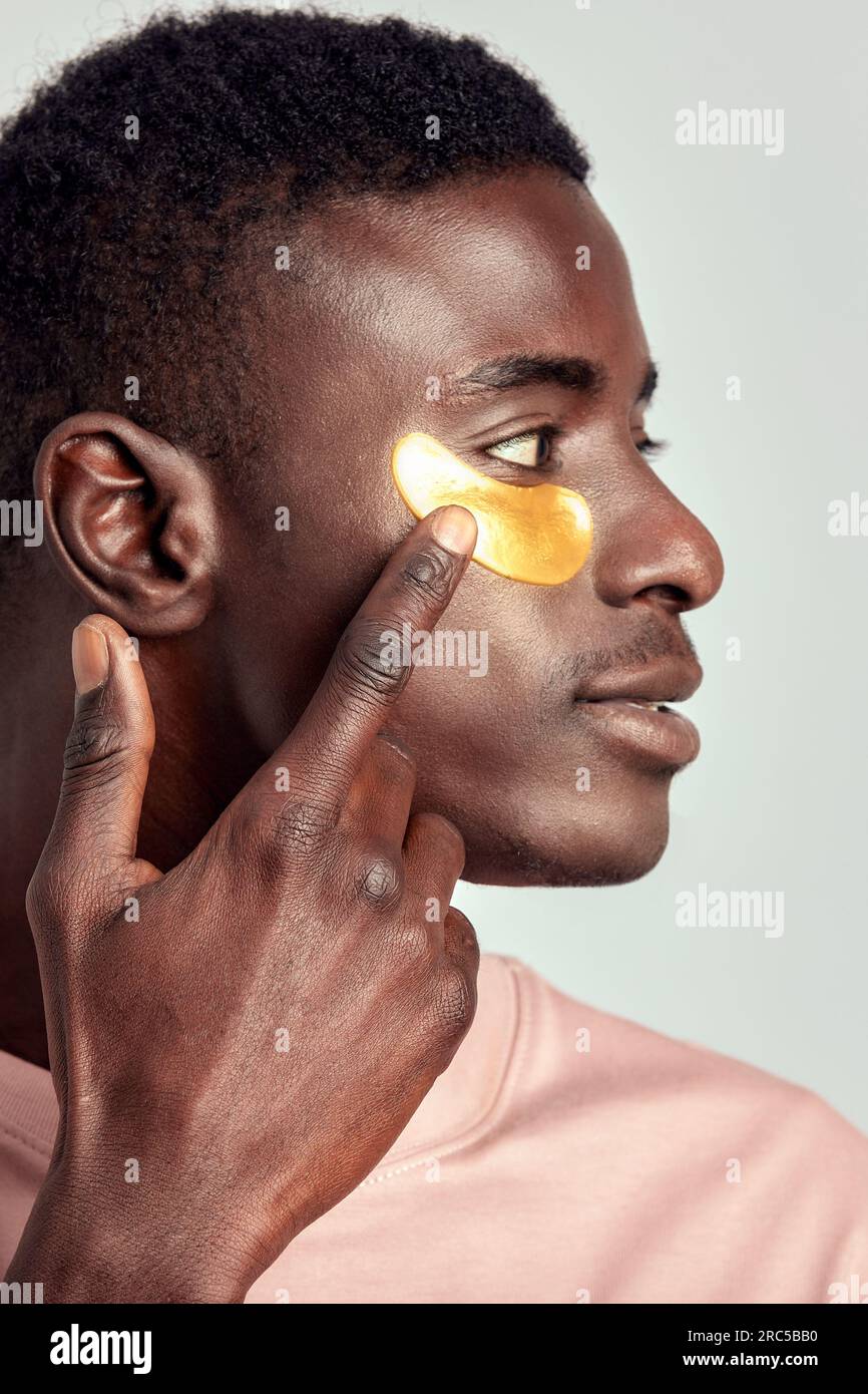 Gros plan portrait d'un jeune beau garçon noir appliquant un cosmétique sous l'oeil hydrogel patch sur son visage. L'homme millénaire afro-américain pratique la peau c Banque D'Images