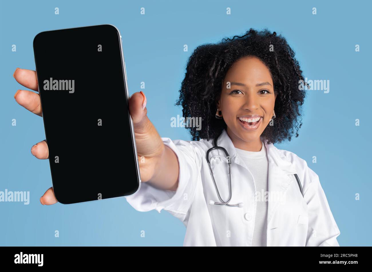 Heureuse jeune femme noire médecin thérapeute en manteau blanc montrer le téléphone avec écran vide Banque D'Images