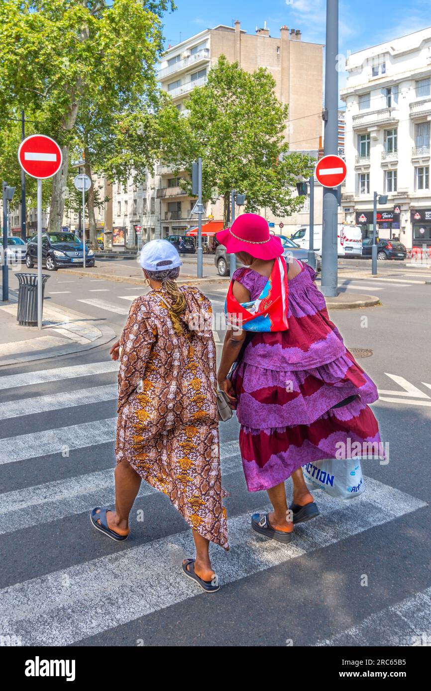 Deux femmes franco-africaines en robes à motifs lumineux traversant la rue du centre-ville sur un passage piétonnier - Tours, Indre-et-Loire (37), France. Banque D'Images