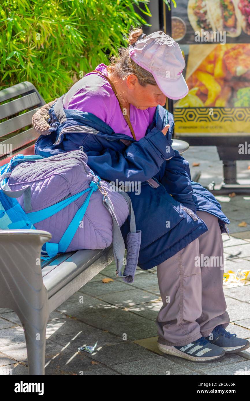 Femme sans abri assise sur un banc du centre-ville avec des effets personnels - Tours, Indre-et-Loire (37), France. Banque D'Images