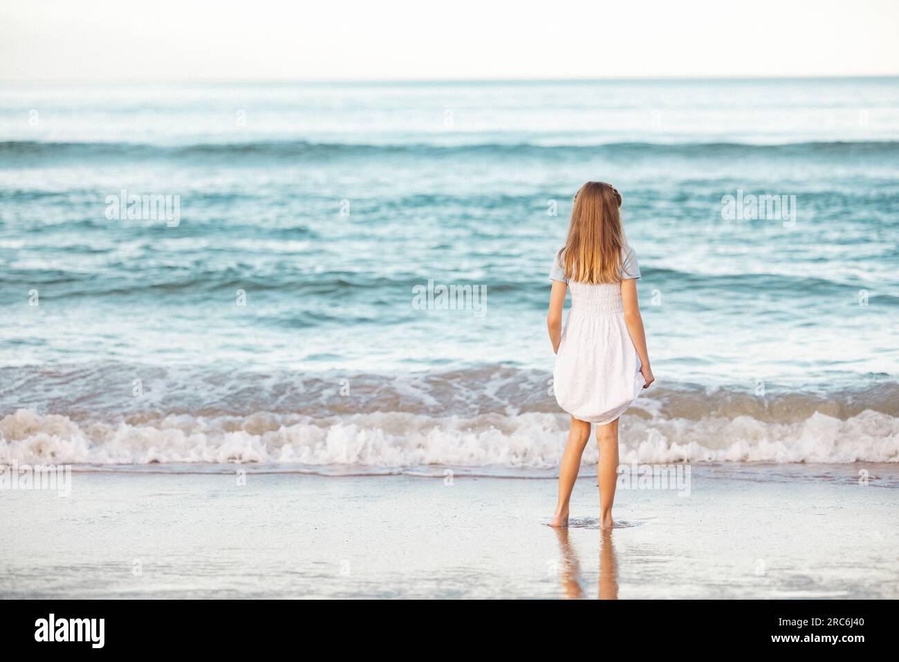 Fille en robe jouant dans les vagues sur la plage. Vue de derrière sans visage. Espace de copie. Banque D'Images
