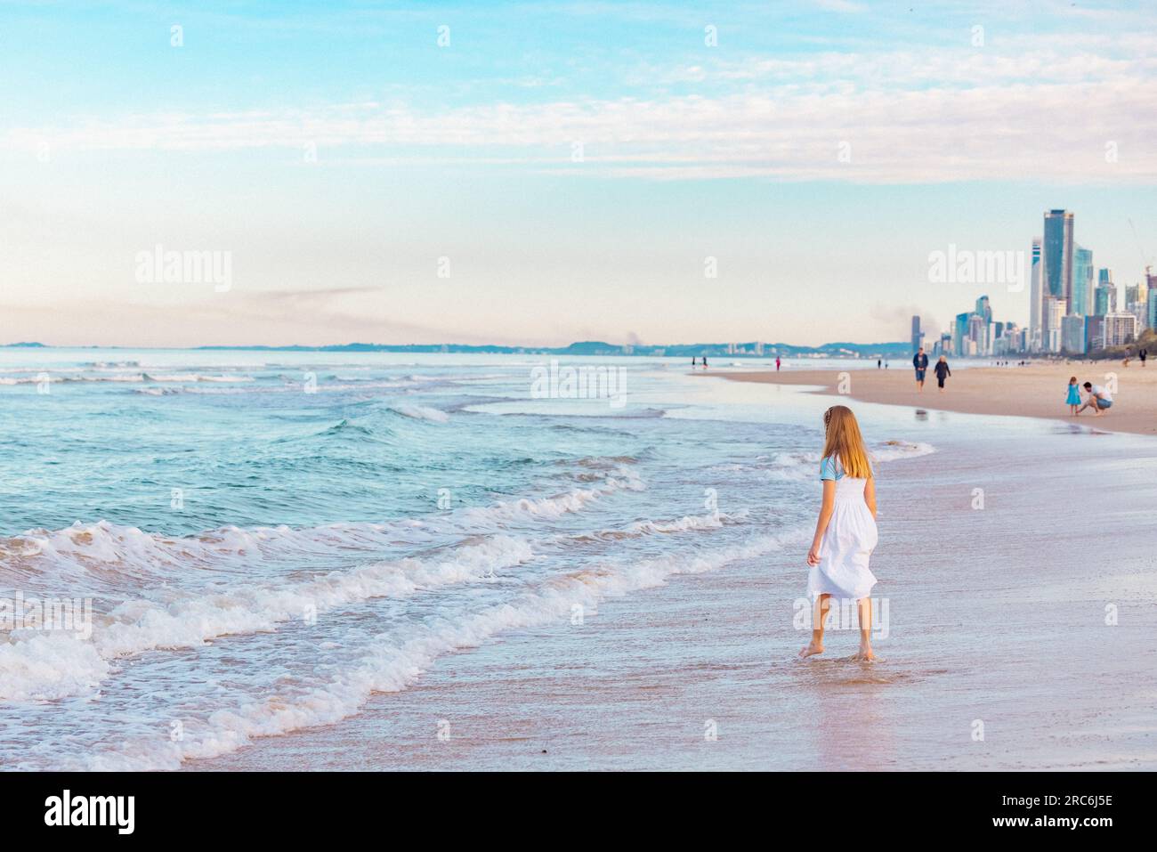 Fille jouant sur la plage éclaboussant dans les vagues en vacances avec la ville Gold Coast Skyline visible en arrière-plan Banque D'Images