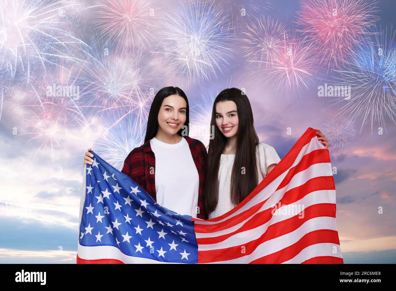 4 juillet - jour de l'indépendance de l'Amérique. Heureuse mère et fille tenant le drapeau national des États-Unis contre le ciel avec des feux d'artifice Banque D'Images