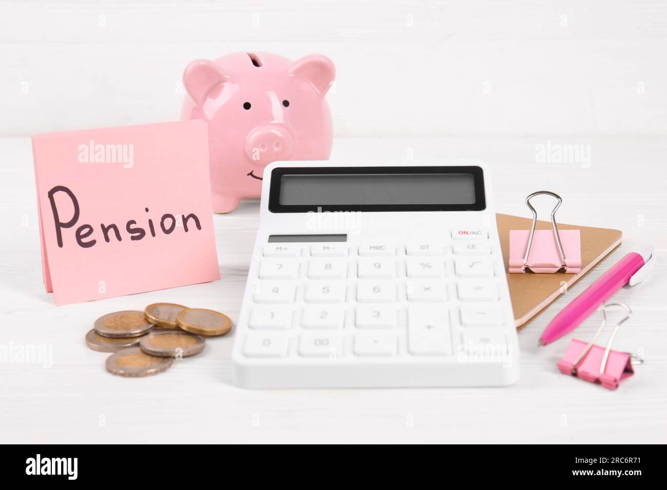 Calculatrice, pièces de monnaie, tirelire, cahier, note avec le mot Pension et stylo sur la table blanche. Concept de retraite Banque D'Images