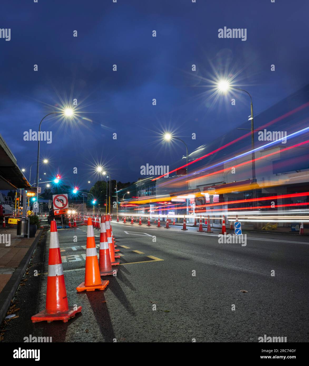 Des cônes orange bordent la route. Sentiers légers d'autobus approchant l'intersection. Travaux routiers à Auckland. Format vertical. Banque D'Images