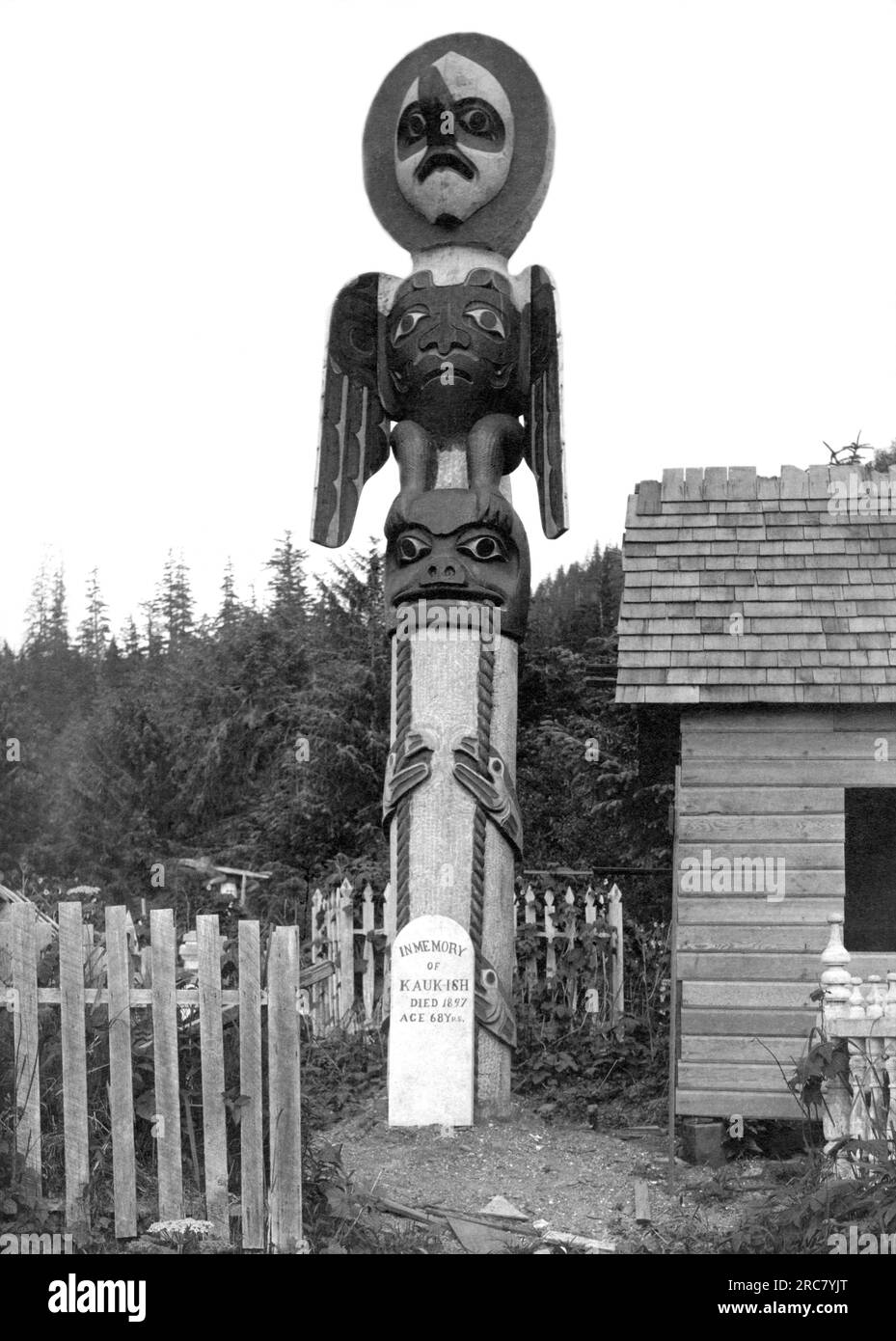 Pi. Wrangle, Alaska : c. 1899. Un totem derrière un marqueur cimétaire qui dit "à la mémoire de Kauk-Ish est mort en 1897 à l'âge de 68 ans". Banque D'Images