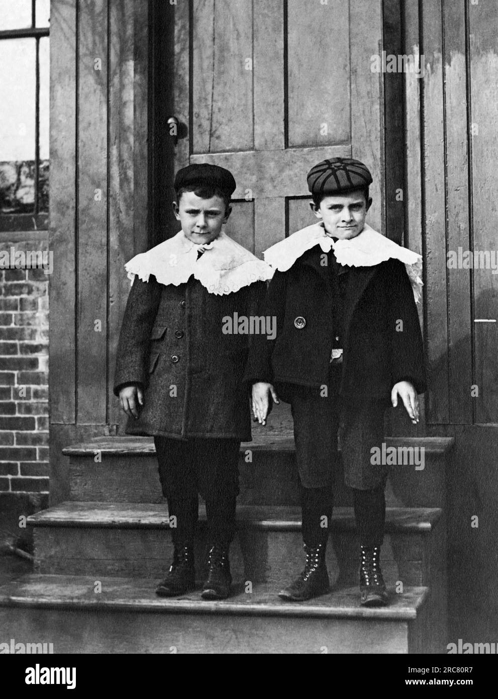 États-Unis : c. 1900 deux jeunes garçons à l'air dur habillés dans leur meilleur dimanche avec des chapeaux et des cols à volants posent sur une porte. Banque D'Images