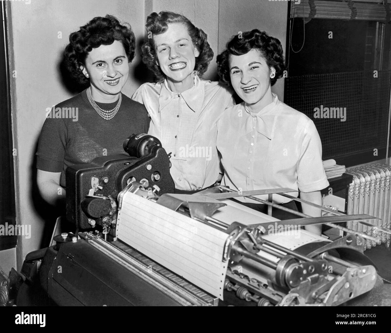 Cleveland, Ohio : février 1951 trois travailleuses de bureau souriantes posent derrière une imprimante d'ordinateur de début. Banque D'Images