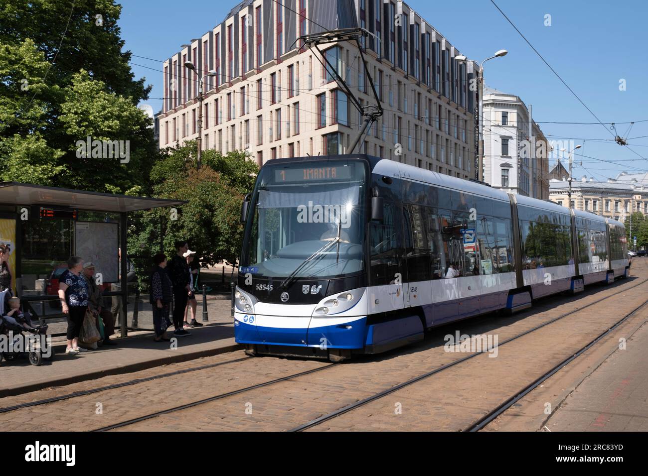 Transports publics Riga. Le tramway électrique bleu et blanc s'arrête à un arrêt où les passagers attendent Banque D'Images