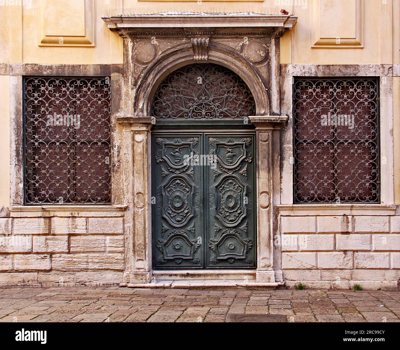 Un vert en bois décoré porte flanquée de deux fenêtres en fer dans le vieux râpé Ghetto de Venise Banque D'Images