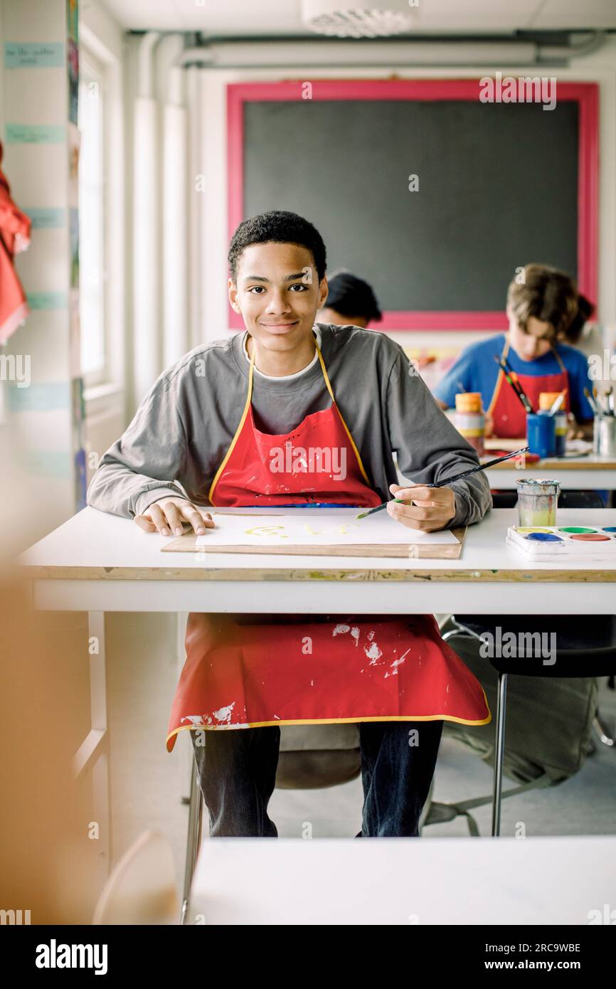Portrait d'un adolescent masculin souriant assis à son bureau pendant un cours d'art au lycée Banque D'Images