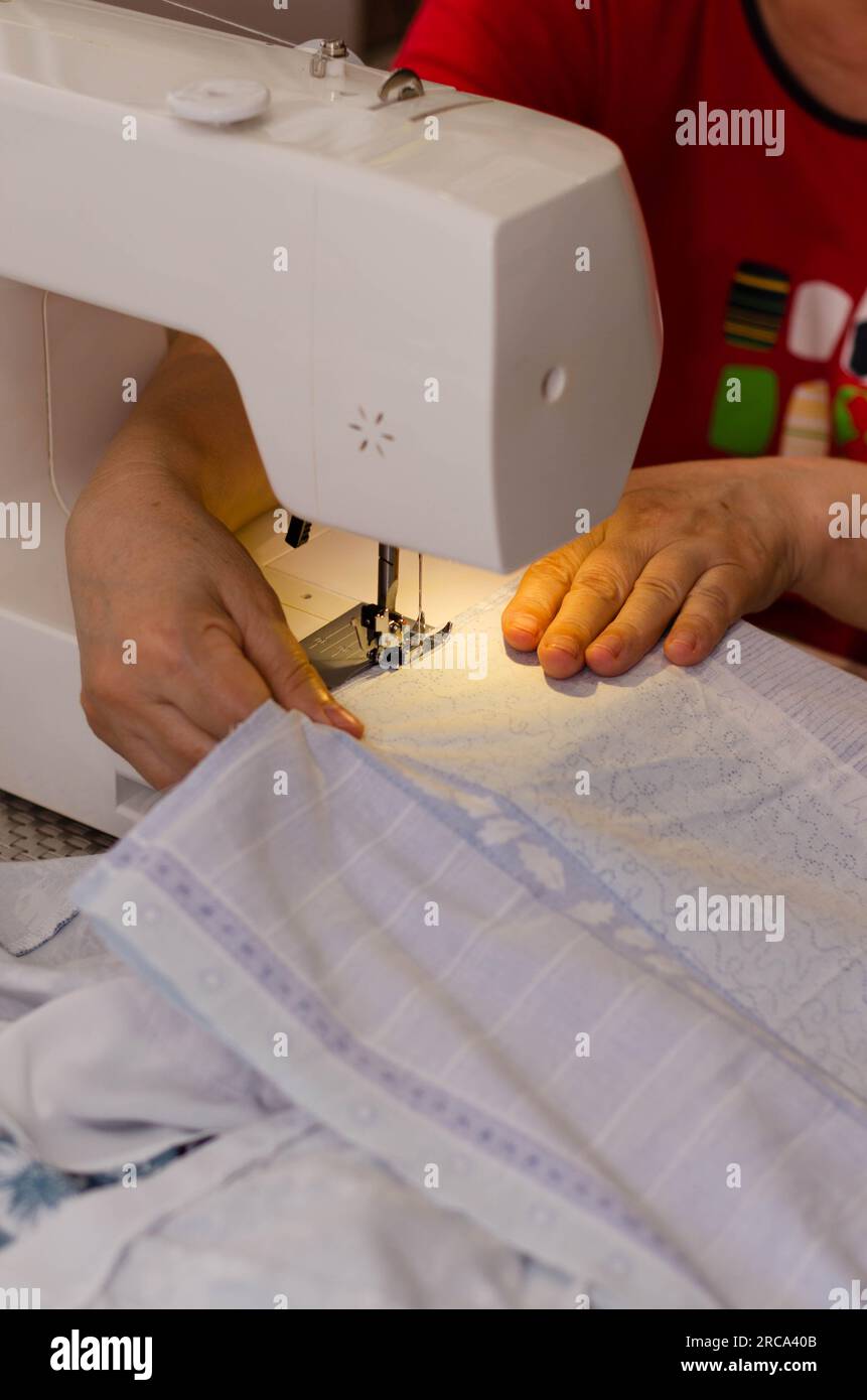 Gros plan des mains d'une couturière cousant du tissu blanc sur une machine à coudre Banque D'Images