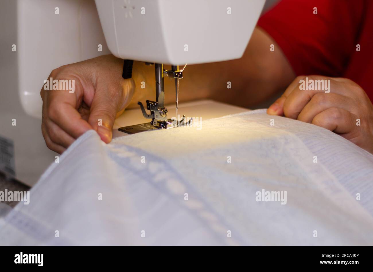 Gros plan des mains d'une couturière cousant du tissu blanc sur une machine à coudre Banque D'Images