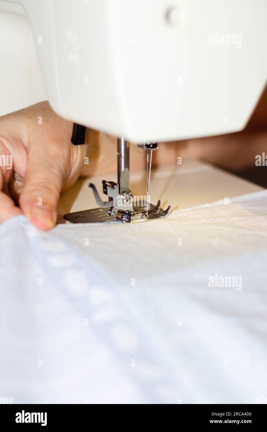 Gros plan des mains d'une couturière cousant du tissu blanc sur une machine à coudre Banque D'Images