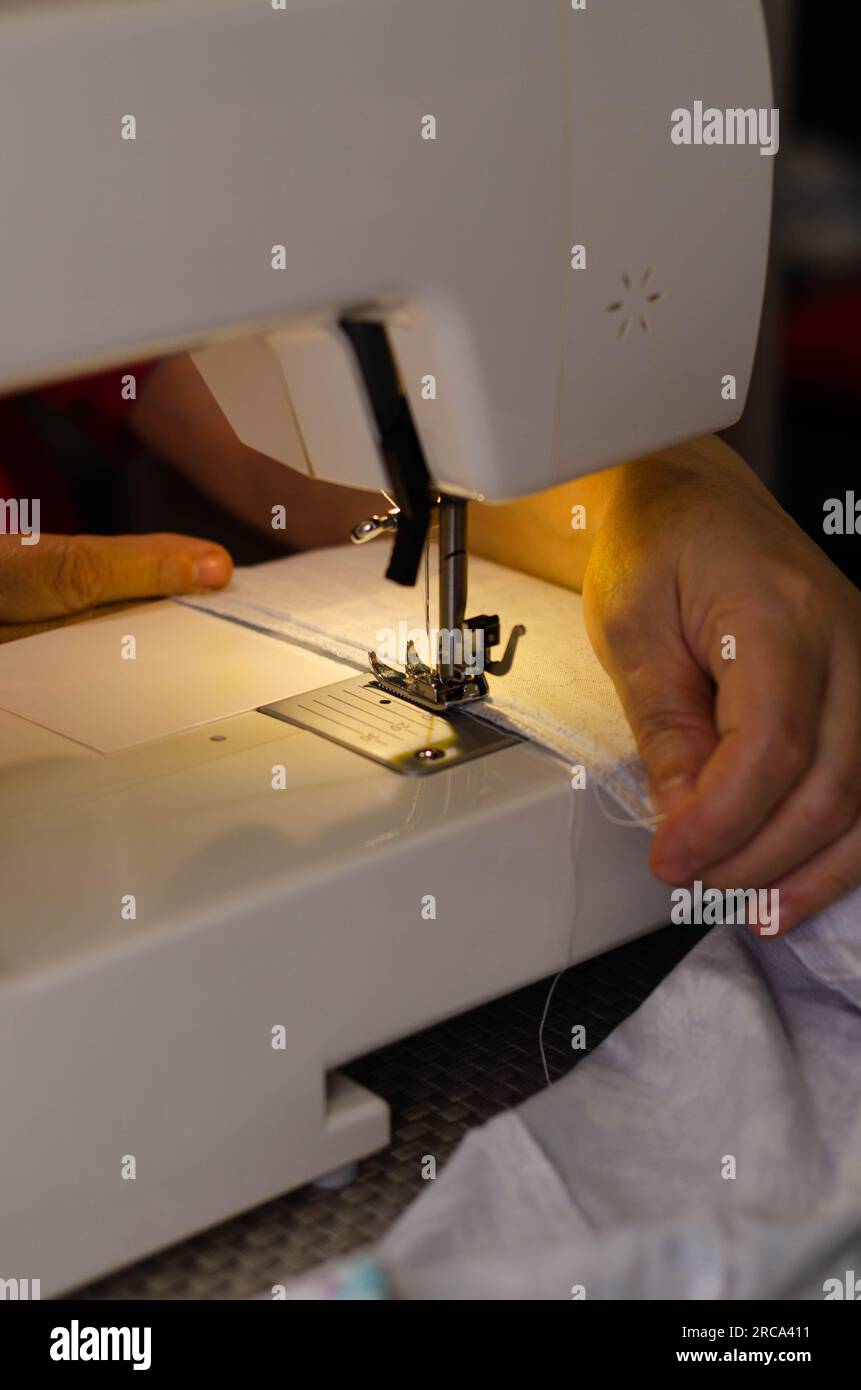 Gros plan des mains d'une couturière cousant du tissu blanc sur une machine à coudre Banque D'Images