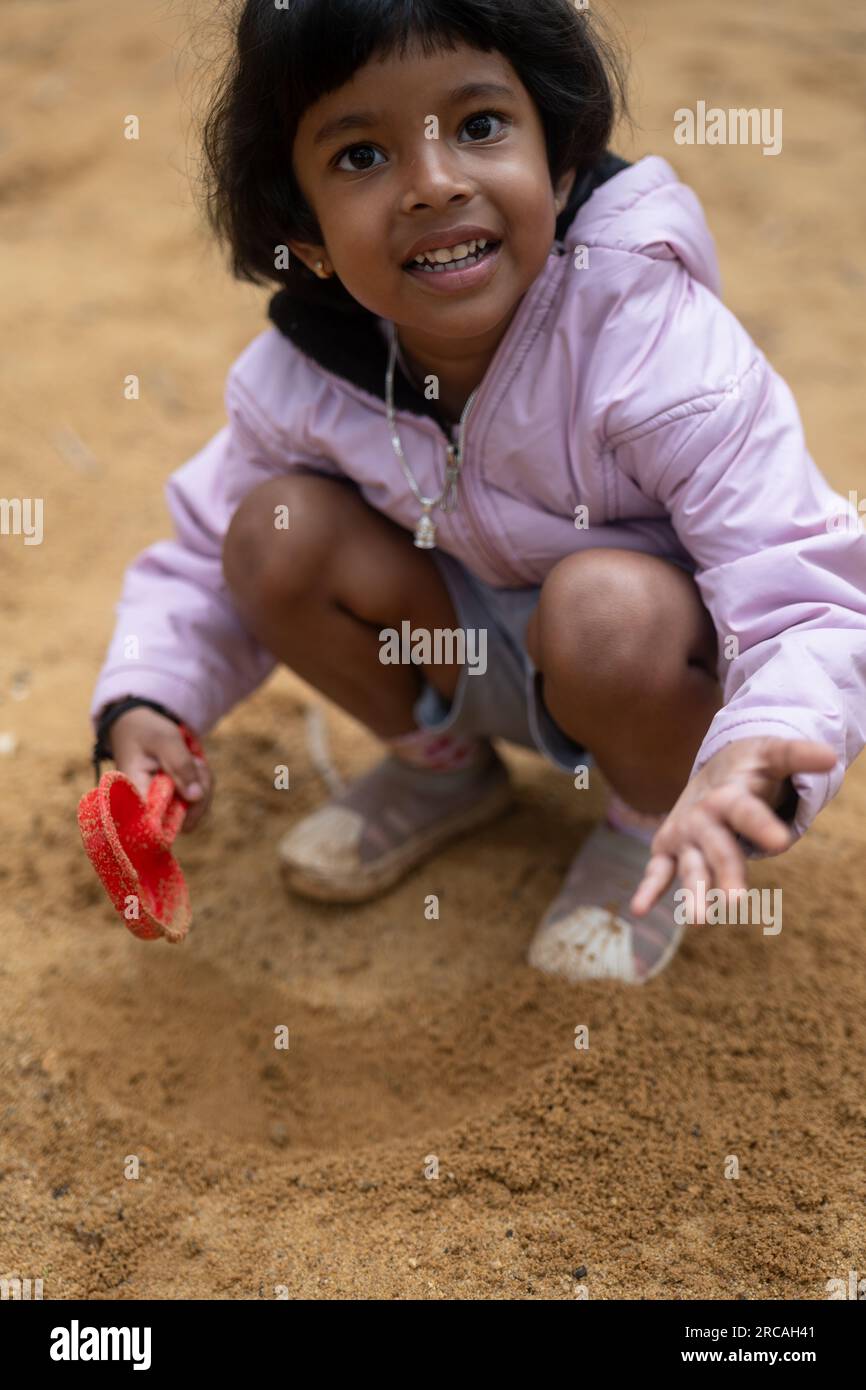 Une petite fille joyeuse joue dans la boue. Elle est couverte de boue et s'amuse beaucoup. Banque D'Images