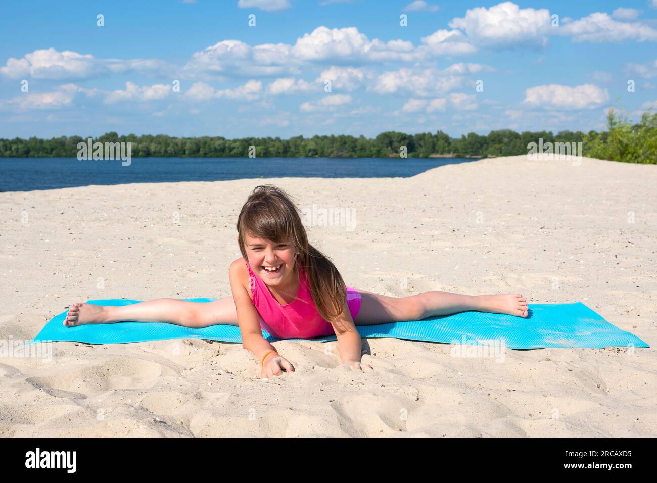 Fille heureuse sur un tapis de yoga faisant de la gymnastique sur la plage. Style de vie actif. Le concept de sport et de jeu actif en été Banque D'Images
