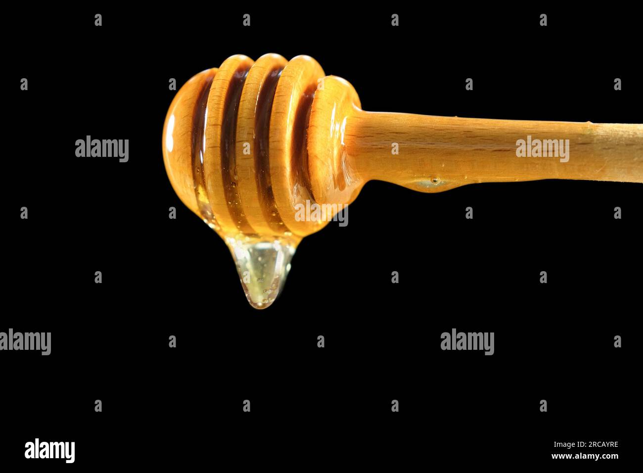 Louche en bois avec du miel égouttant isolé sur fond noir, produits apicoles naturels biologiques Banque D'Images