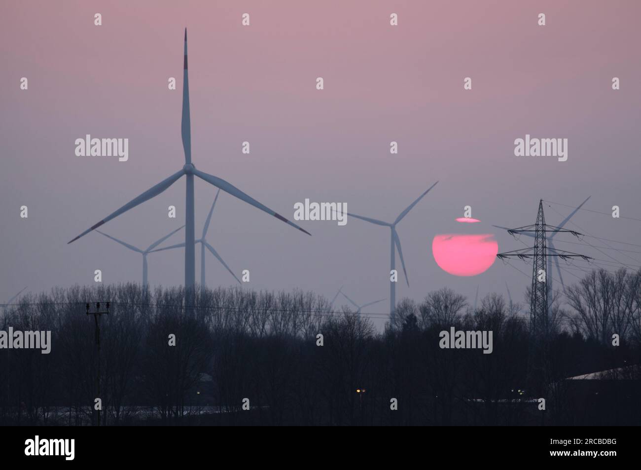 Un soleil d'hiver brumeux se couche derrière des éoliennes près de Grevenbroich, en Allemagne. Banque D'Images