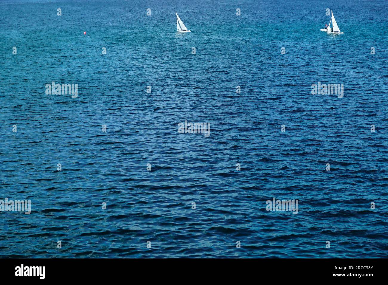 Deux petits voiliers dans une vaste mer bleue ouverte. Banque D'Images