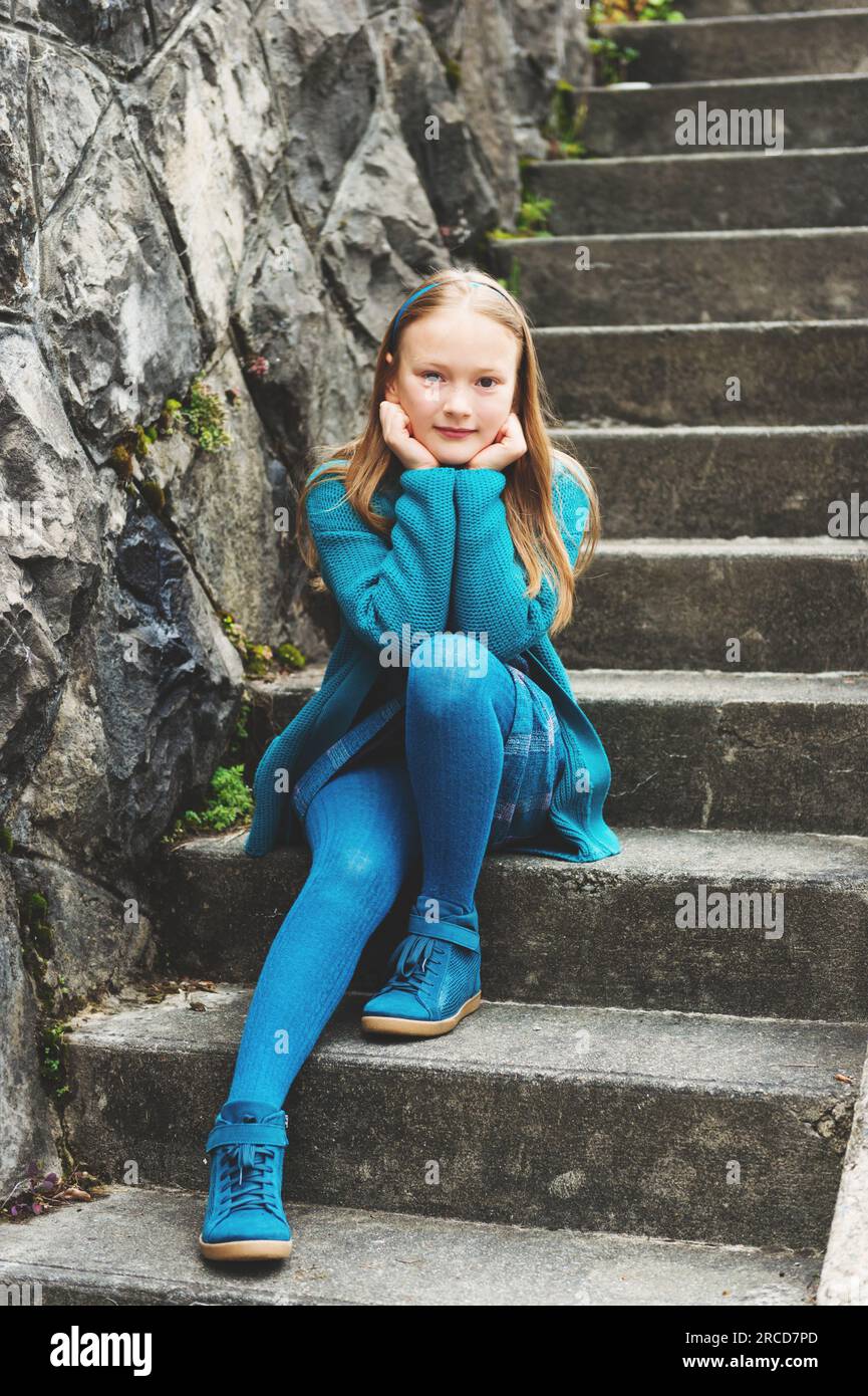 Portrait de mode en plein air d'adorable petite fille de 8-9 ans, portant des vêtements bleus et des chaussures, assis dans les escaliers dans une ville Banque D'Images