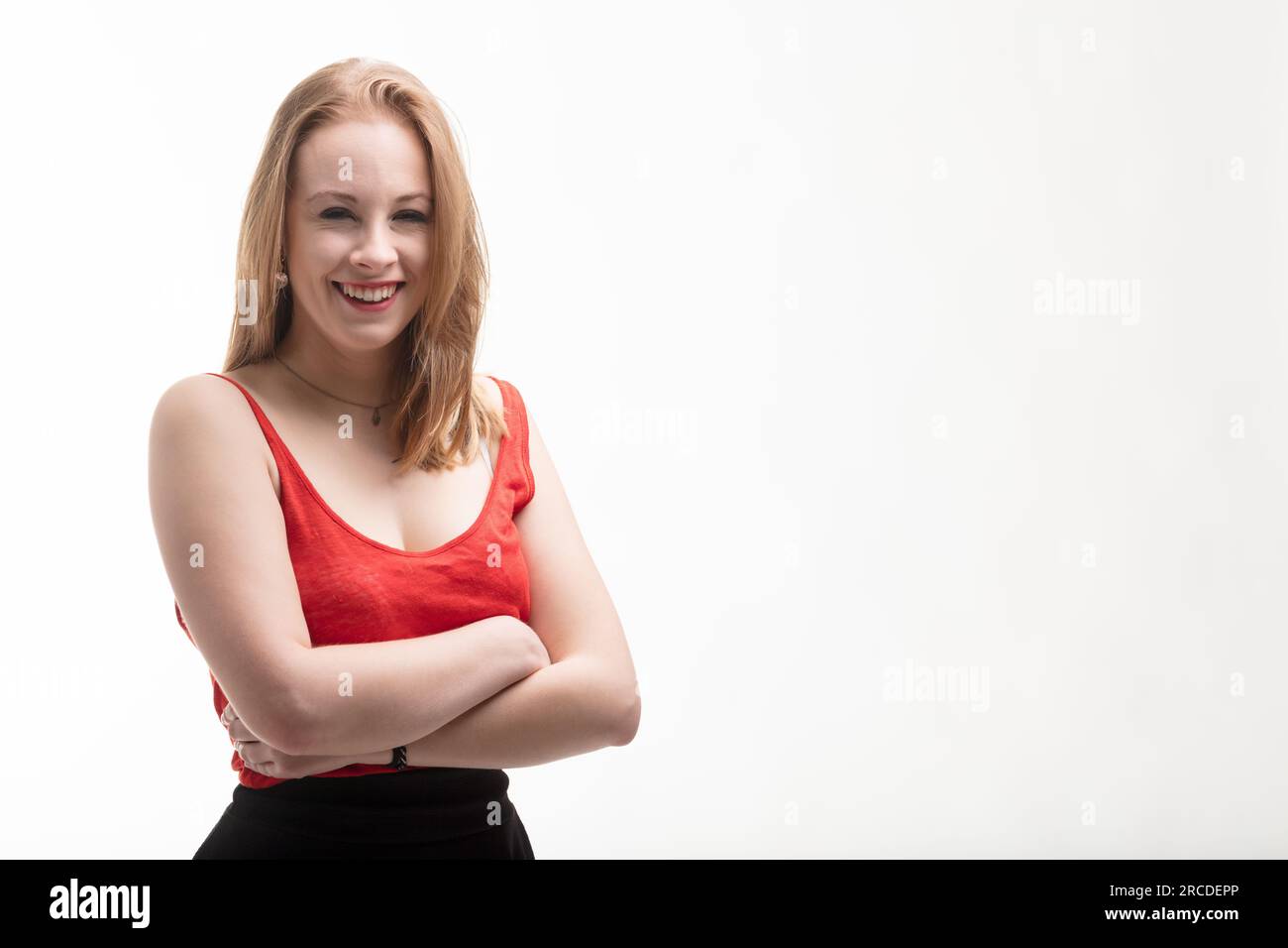 Jeune femme avec la peau très claire et les cheveux blonds rougeâtres porte une robe rouge vif. Elle croise les bras, sourit, puis rit. Son regard est accustome Banque D'Images