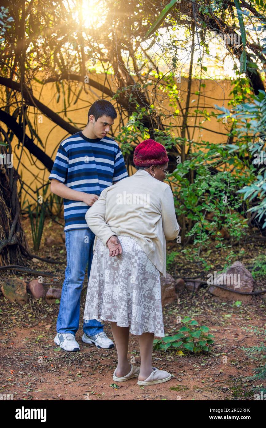 vieille dame africaine à la retraite marchant dans le jardin d'arrière-cour avec un adolescent Banque D'Images