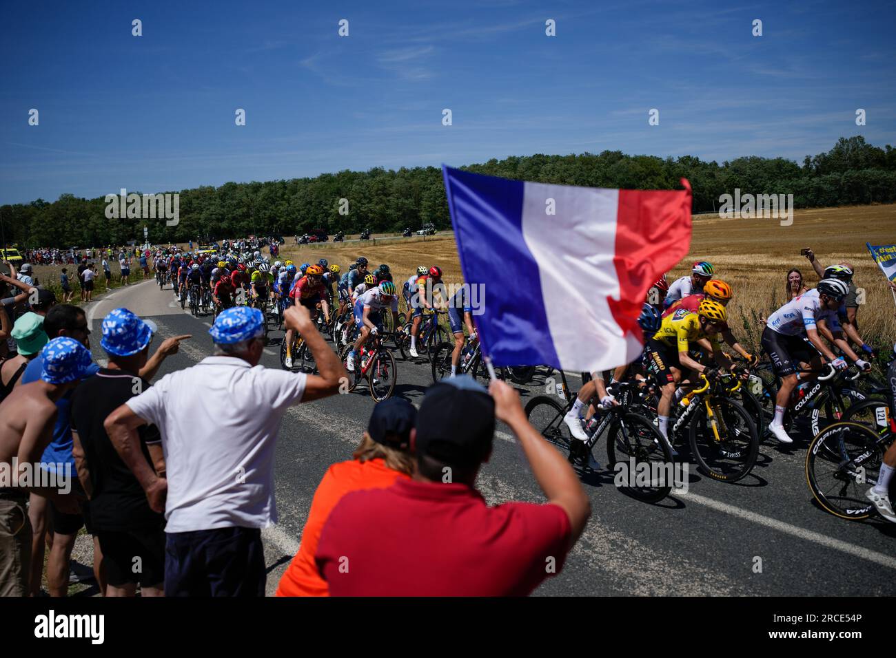 On Bastille Day, the anniversary of the storming of Bastille prison in 1789, now a French national holiday, a cycling fan waves the national flag as Denmark's Jonas Vingegaard, wearing the overall leader's yellow jersey, passes in the pack during the thirteenth stage of the Tour de France cycling race over 138 kilometers (86 miles) with start in Chatillon-sur-Chalaronne and finish on Grand Colombier pass, France, Friday, July 14, 2023. (AP Photo/Daniel Cole) Banque D'Images