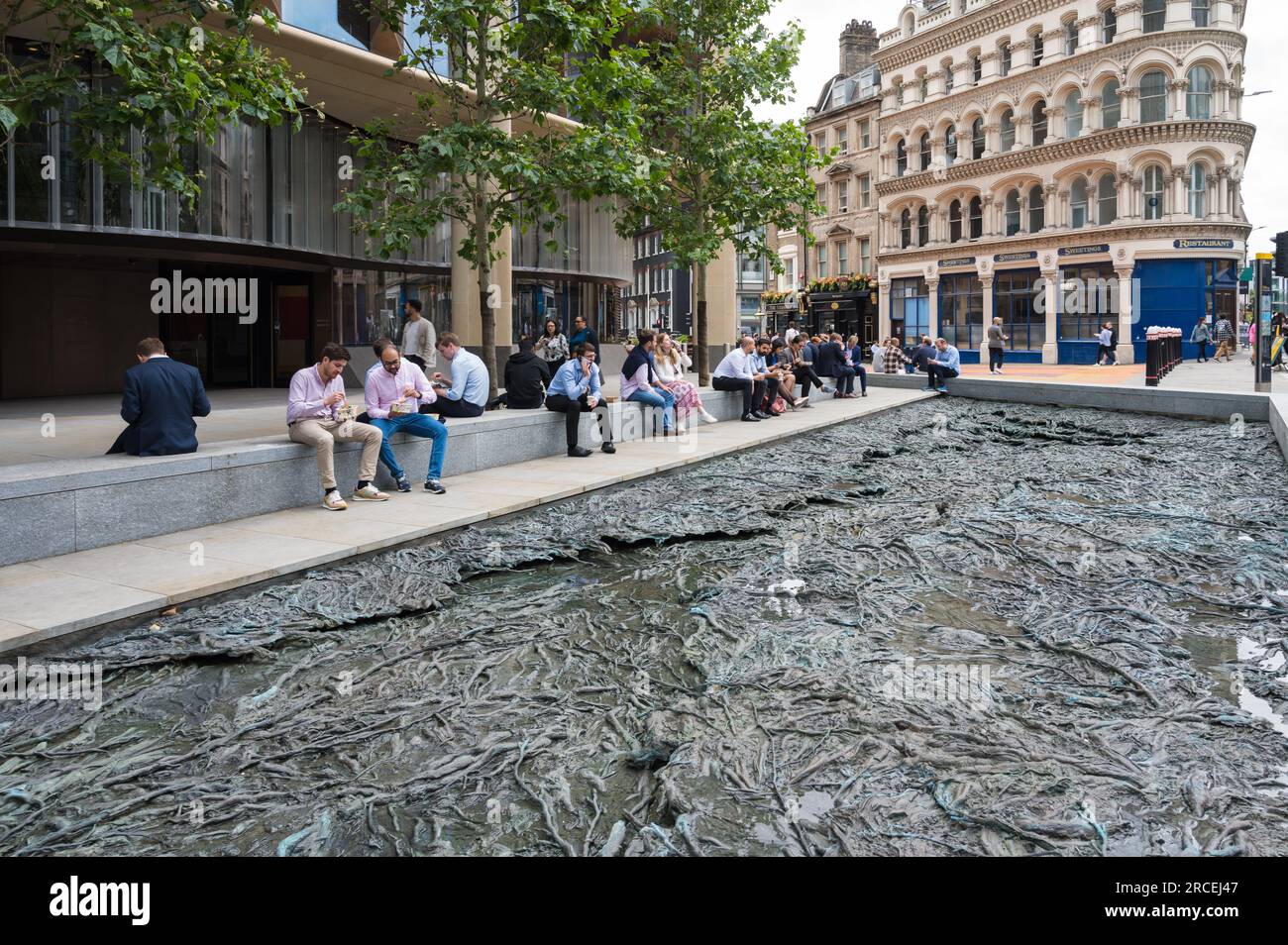 Les employés de la ville en pause déjeuner assis à côté d'une piscine "ruisseaux oubliés" par Cristina Iglesias à l'extérieur de l'immeuble de bureaux du siège de Bloomberg. Londres, Royaume-Uni Banque D'Images